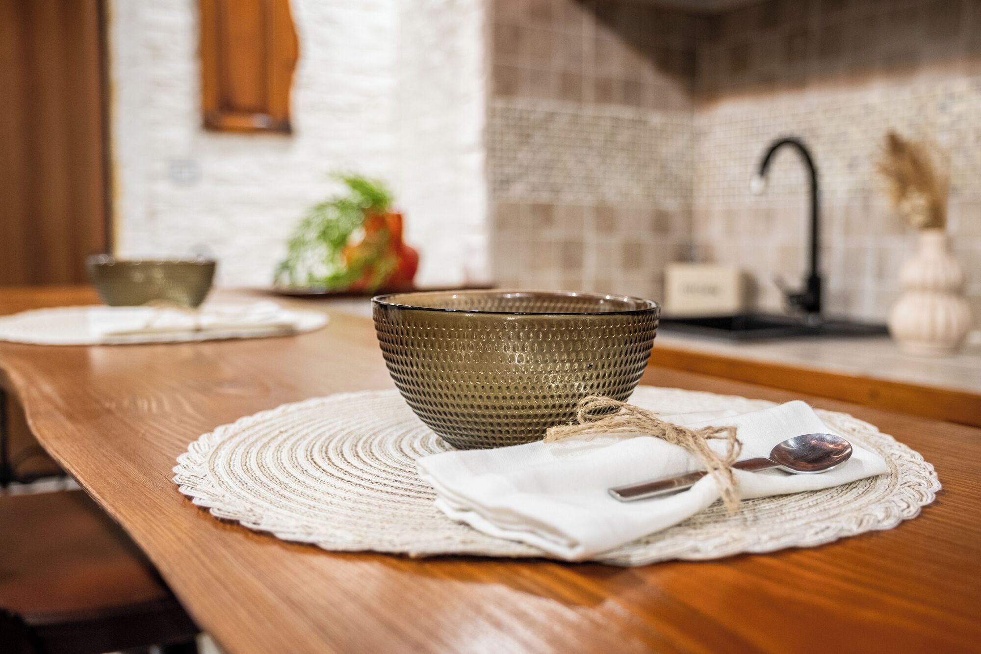 A wooden table with a textured placemat, a bowl, a spoon, and a cloth tied with twine.
