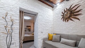 A modern living room with a stone wall, a sofa with cushions, a decorative sun sculpture, and a view into another room. - Su Lizu, charm and relaxation in the historic center of Cagliari - with patio. (Cagliari)