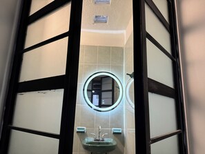 A bathroom with a round mirror, a sink, and frosted glass doors. - Minimalist loft 3 blocks from the Zocalo (Oaxaca de Juárez)
