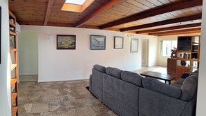 Ein geräumiger Wohnbereich mit hoher Decke, Holzbalken, einem grauen Sofa, einem Couchtisch und einem Bücherregal.