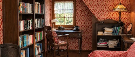 Una habitación acogedora con un escritorio de madera, estanterías, un sofá rojo con estampado y un ventanal con vistas.