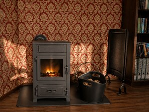 A wood-burning stove with a glass door, a black storage basket, and a bookshelf with books. - A stylish retreat in the Art Deco/Art Nouveau style with an English cottage vibe (Wurzbach)