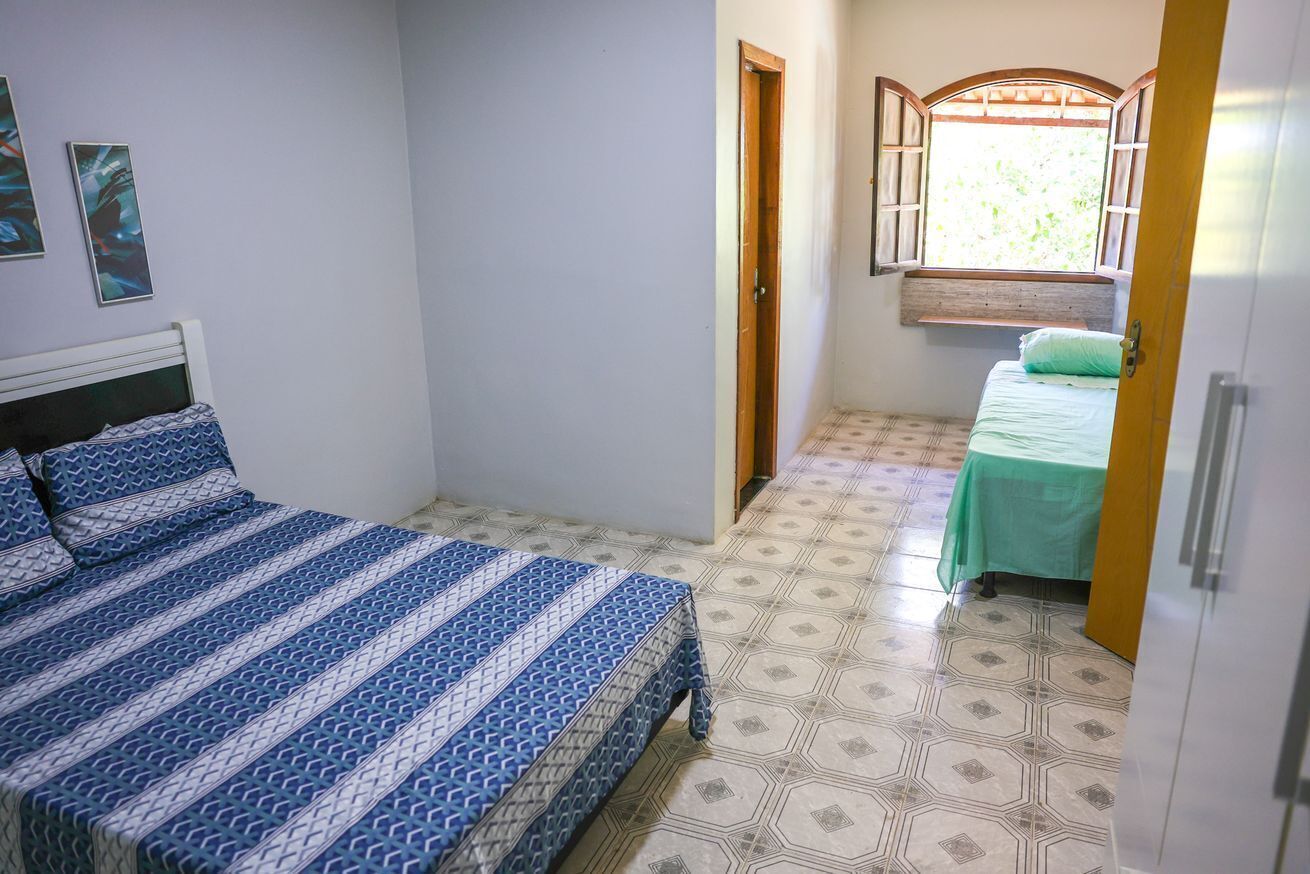 Un dormitorio con una cama, un ventanal con contraventanas abiertas y una mesa verde con mantel.