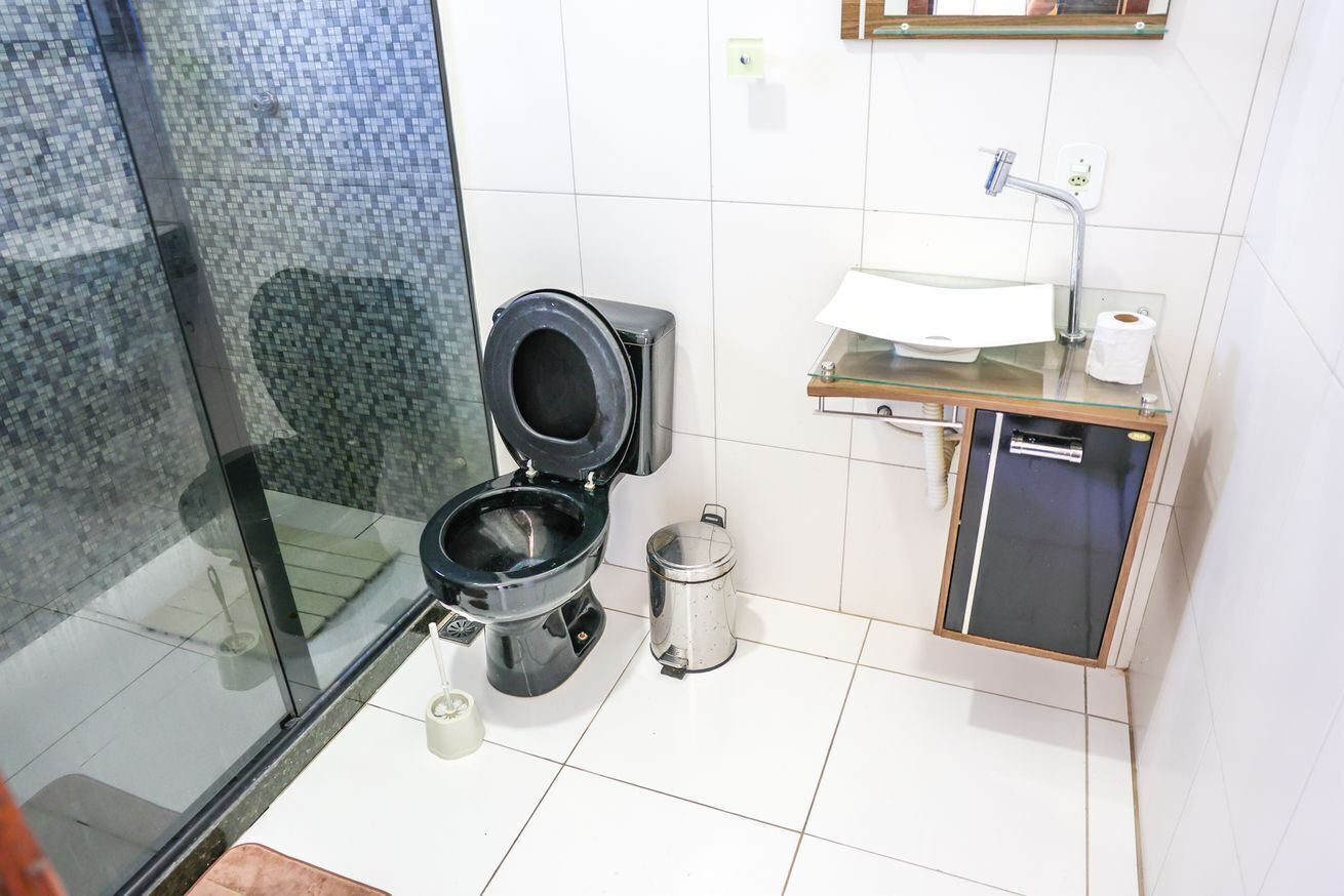 A compact bathroom with a glass shower enclosure, a black toilet, a small trash bin, and a glass-topped sink with a mirror above it.