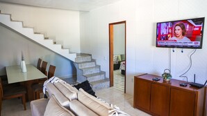 Una sala de estar con sofá, mesa de comedor y televisor montado en la pared.