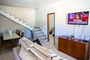 Ein Wohnzimmer mit einer Couch, einem Esstisch und einem an der Wand befestigten Fernseher.