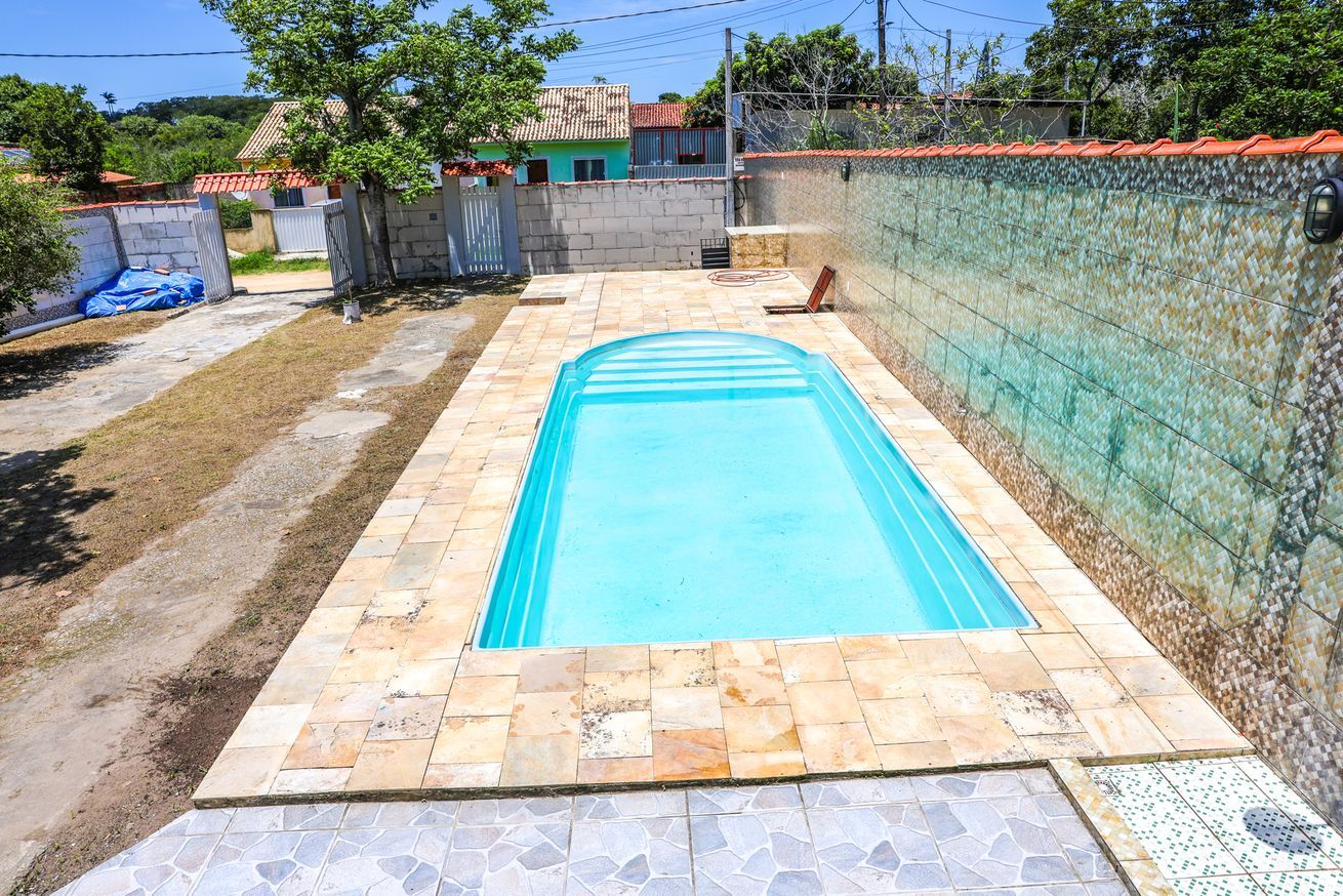 A rectangular swimming pool with a tiled deck, surrounded by a low wall and a fence.
