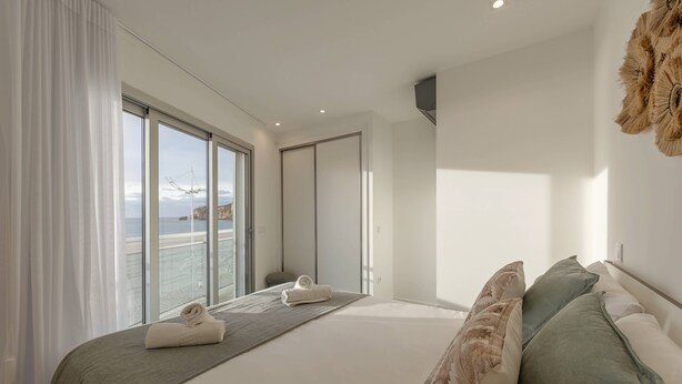 Una camera da letto moderna con un letto grande, vista sul mare e una porta scorrevole che dà su un balcone.