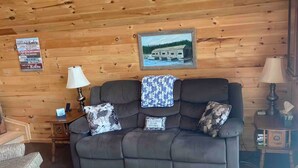 L’intérieur chaleureux d’un chalet avec un plafond en bois, un canapé avec des coussins, un tapis à motifs et un tableau encadré au mur.