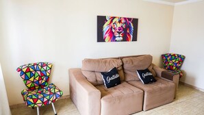 Ein Wohnzimmer mit einem beigefarbenen Sofa, zwei bunten Sesseln und einem lebendigen Löwenbild an der Wand.