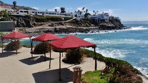 A coastal beach with red umbrellas and a white building in the background. - Beautiful Luxury penthouse in Rosarito beach (B.C.)