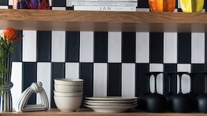 A kitchen with black and white checkered backsplash, wooden shelves, and various kitchenware.