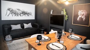 A modern living room with a black sofa, a wooden dining table set for four, and artwork on the walls.