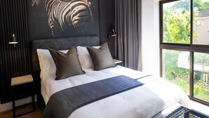 A modern bedroom with a large bed, dark curtains, a zebra mural, and a view of greenery outside.