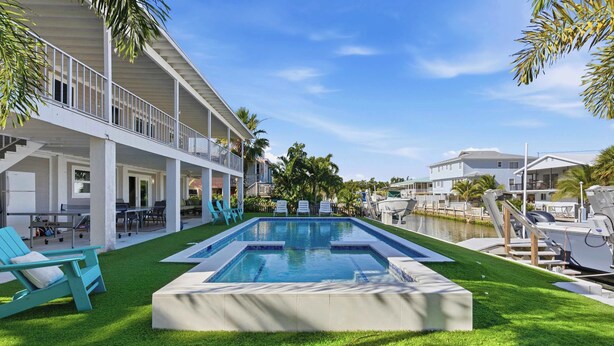 A swimming pool with a deck, surrounded by grass and palm trees, with a building in the background. - Hooked on Avocado -Stunning 5 Bedroom/ 3 Bath waterfront home on canal, resort style private pool & hot tub, 34’ dock, and quick open-water Gulf and Atlantic access. Ice Maker, Ping Pong table. Minutes to Sombrero Beach & Dining. (Marathon)