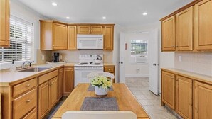 A compact kitchen with wooden cabinets, a white stove, and a dining table with a vase of flowers. - The Bungalow 1 Bed / 1 Bath Duplex Near Vanderbilt Beach (Naples)