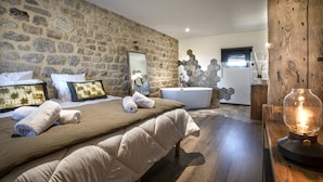 Quarto com parede de pedra, uma cama grande com cabeceira, uma banheira e um armário de madeira.