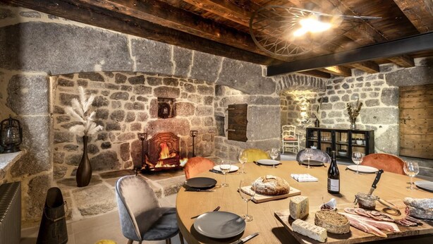 Uma sala de jantar rústica com lareira de pedra, vigas de madeira e uma mesa posta para refeição.