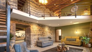 Uma sala de estar espaçosa com parede de pedra, escada de madeira, um sofá cinzento, um sofá amarelo e uma mesa de centro de madeira.