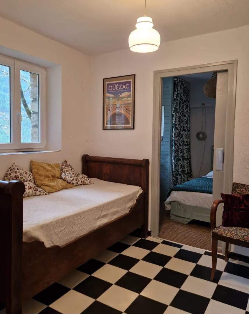 Een slaapkamer met een bed, een stoel, een geruit vloertapijt, een poster aan de muur en een raam.