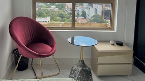Ein Zimmer mit einem großen Fenster, einem roten Sessel, einem kleinen runden Tisch und einer Marmorvase.