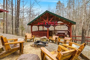 A wooden outdoor seating area with a barbecue grill, surrounded by trees. - Smoky Mtn Cabin w Hot Tub & Game Room! (Sevierville)