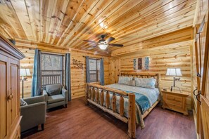 A wooden cabin bedroom with a bed, a chair, a nightstand, and a ceiling fan. - Smoky Mtn Cabin w Hot Tub & Game Room! (Sevierville)