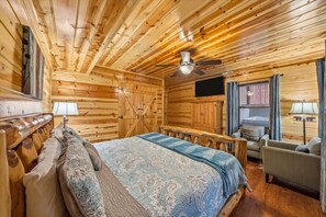 A log cabin bedroom with a bed, a chair, a television, and a ceiling fan. - Smoky Mtn Cabin w Hot Tub & Game Room! (Sevierville)