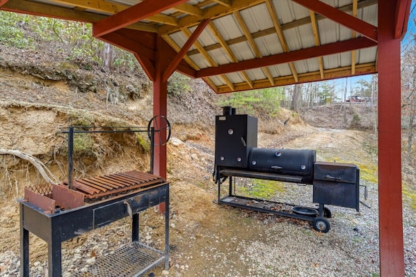 Et udendørs grillområde med grill og røgeovn under et overdækket område.