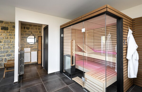 A modern bathroom with a glass shower enclosure, a wooden bench, and a stone wall.