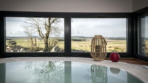 Une salle de bain moderne avec un jacuzzi entouré de parois de verre, une lanterne en bois et un objet sphérique rouge posé sur le sol.