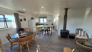 Un amplio salón con una mesa de comedor, sillas de mimbre, un sofá, una chimenea y una cocina al fondo.