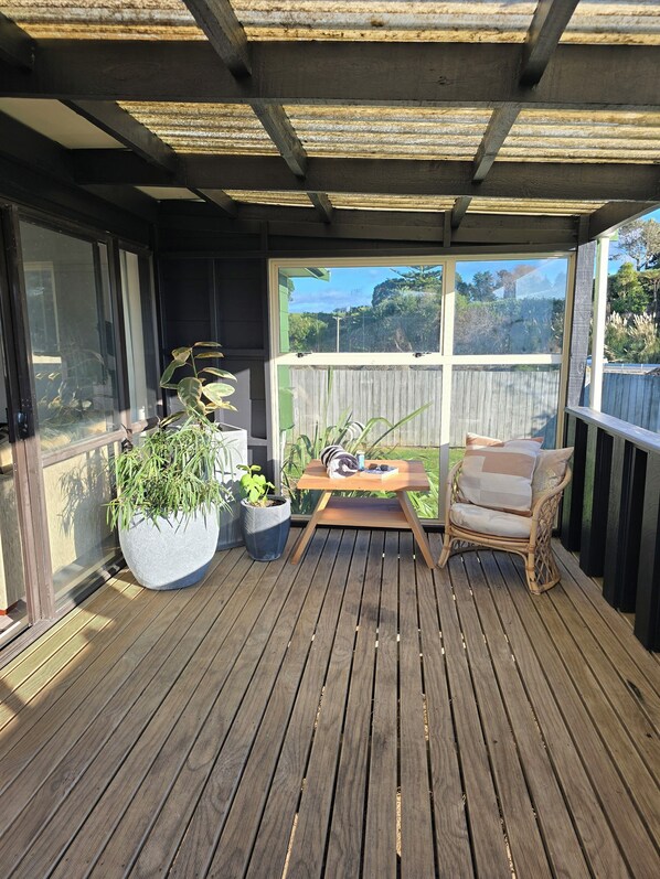 A wooden deck with a table and chair, potted plants, and a view of the surrounding area.