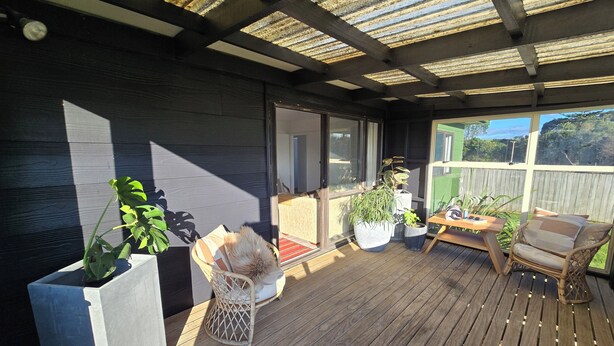 Un espacio al aire libre techado con piso de madera, plantas en macetas y mobiliario para sentarse.