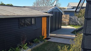 Una propiedad residencial con una casa de color oscuro, una terraza de madera y un pequeño jardín.