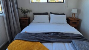 Un dormitorio con una cama, dos mesitas de noche, una ventana con vistas a árboles y una cortina.