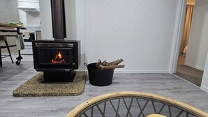 Una sala de estar moderna con una estufa de leña, un comedor y una cocina al fondo.