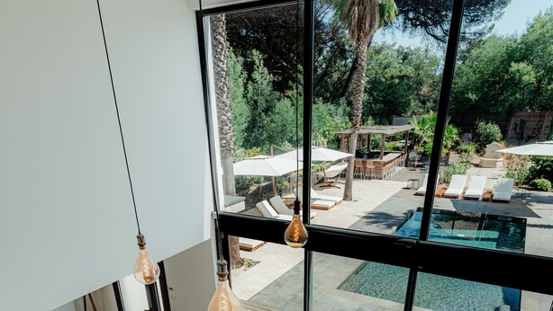 Un intérieur moderne avec un escalier menant à un balcon d’où l’on a vue sur une piscine et un jardin.