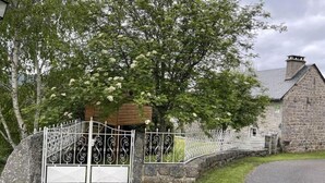 A stone building with a metal gate, surrounded by trees and a paved path. - L'Oustal de la Fillo (CHAUCHAILLES)