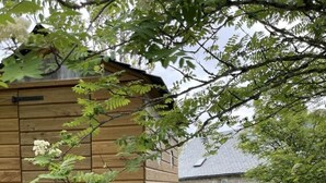 A wooden structure with a ladder, a stone building, and a grassy yard. - L'Oustal de la Fillo (CHAUCHAILLES)