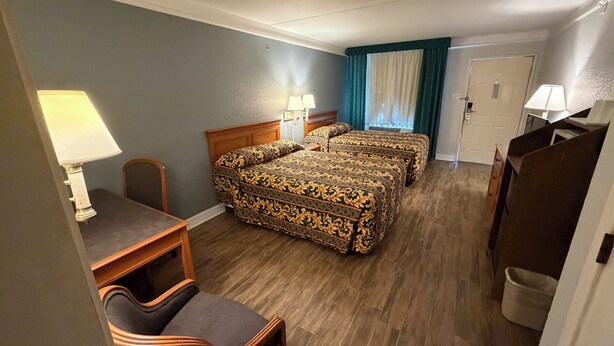 Une chambre d’hôtel avec deux lits, un bureau, une chaise, une lampe et une porte.