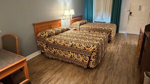Une chambre d’hôtel avec deux lits, une tête de lit en bois, un bureau, une chaise, une lampe et une porte.