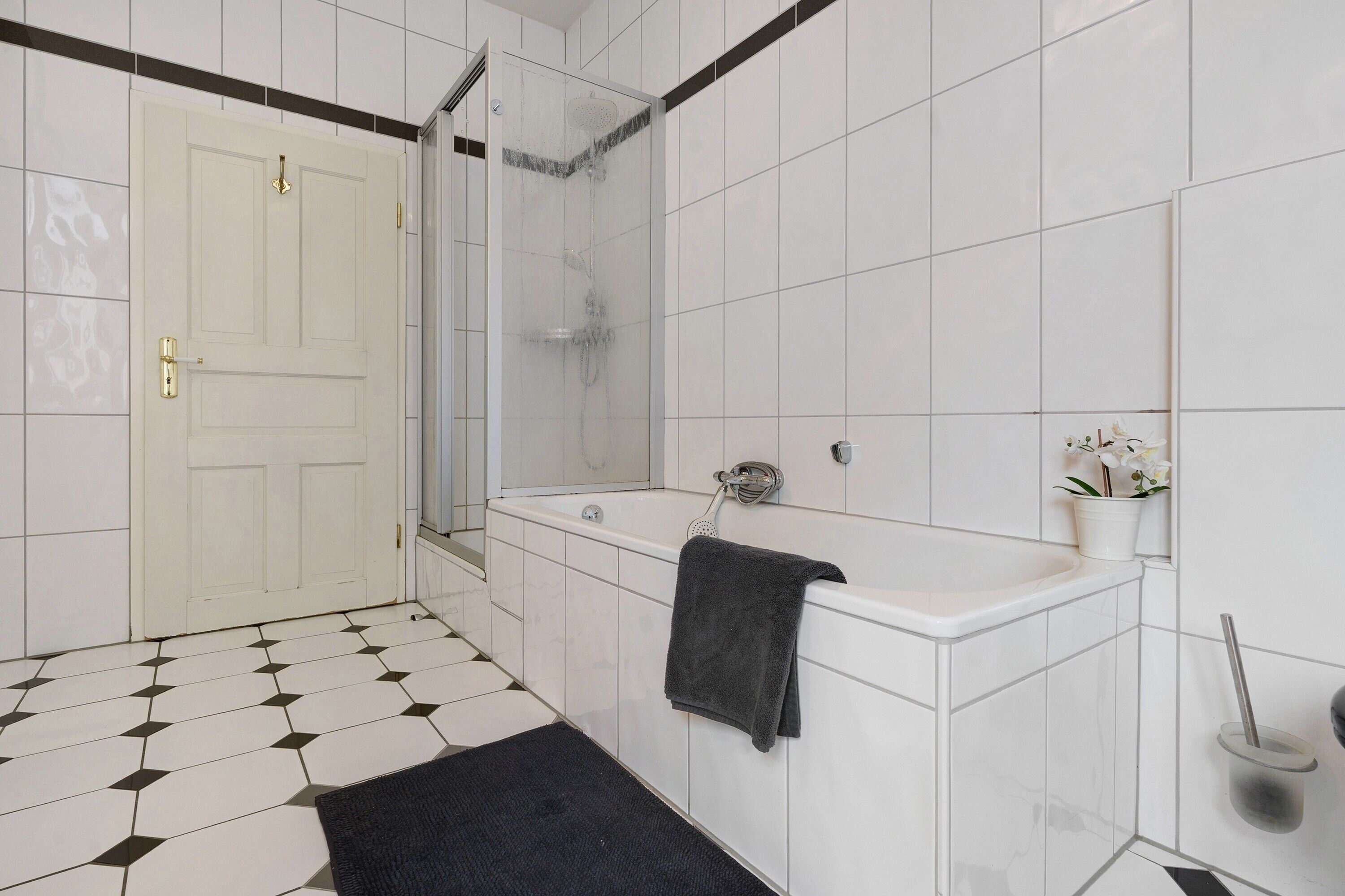 Een badkamer met een witte deur, een badkuip, een douche en een zwarte badmat.
