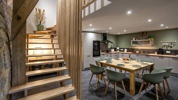 A modern kitchen with a dining area, featuring a wooden staircase, a dining table with chairs, and a kitchen island.