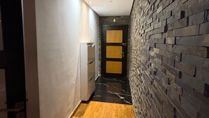 A narrow hallway with wooden flooring, a white wall on one side, and a textured stone wall on the other.