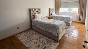 A bedroom with two beds, a large window with curtains, and a patterned rug.