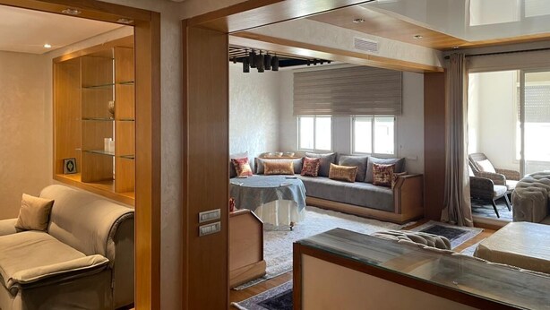 A modern hotel room with a sofa set, a dining table, and a wooden bookshelf.