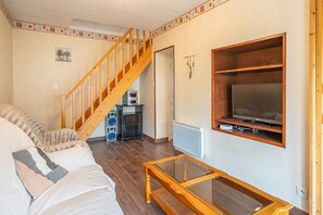 A living room with a wooden staircase, a sofa, a coffee table, and a TV mounted on the wall. - Holiday Home 'La Maison Charentaise' with Private Terrace and Wi-Fi (Saint-Simon de Pellouaille)