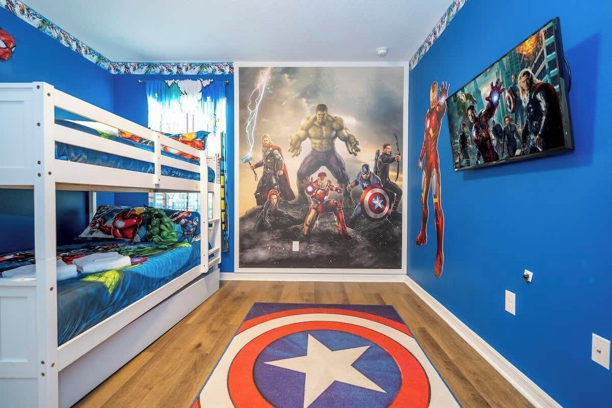 A room with a bunk bed, a Captain America themed rug, and a large Avengers movie poster on the wall.