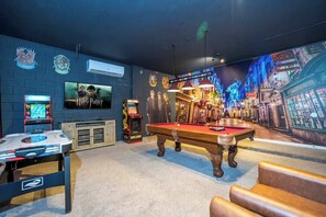 Una habitación con mesa de billar, juegos de arcade y un gran mural en la pared.